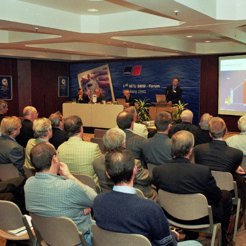 A presentation with a screen; the audience sits in multiple rows and listens attentively