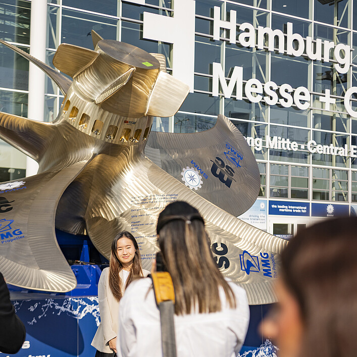 Großes Schiffspropeller‑Exponat vor dem Eingang der Hamburg Messe, mehrere Personen im Vordergrund; auf der Glasfassade steht „Hamburg Messe + Congress“.