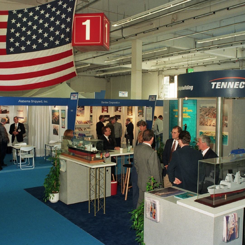 Several exhibition stands with visitors; a USA flag is hanging from the ceiling