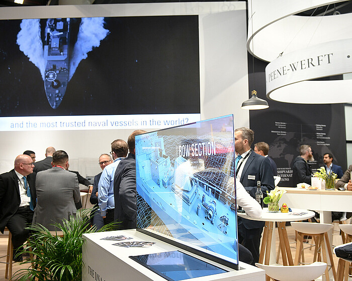 A glass pane with a "hologram" of a ship. A group of men in suits sitting in the background.