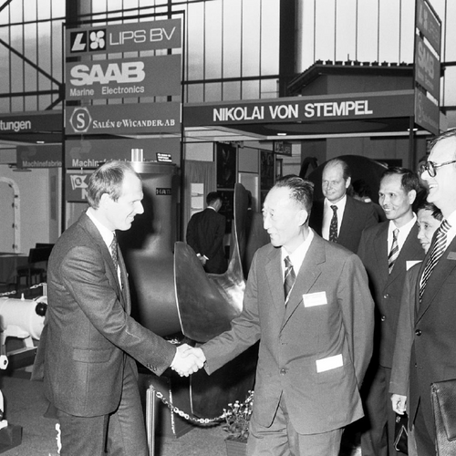 A black-and-white photograph from an earlier trade fair, showing two men shaking hands