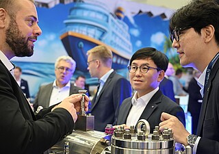 Aufnahme von einem Austeller und zwei Besucher im Gespräch. 