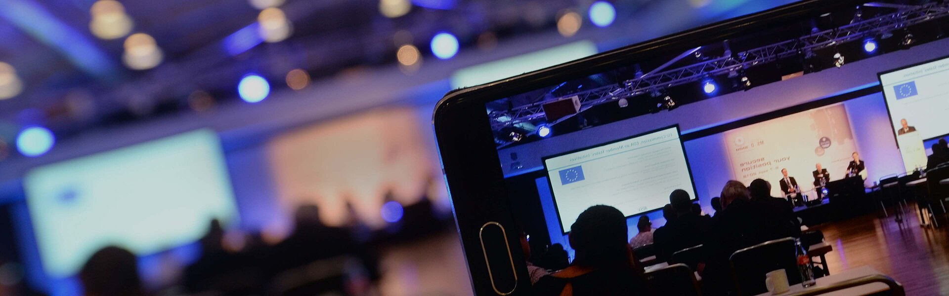 A sharp phone in the foreground filming the blurry stage in the background.