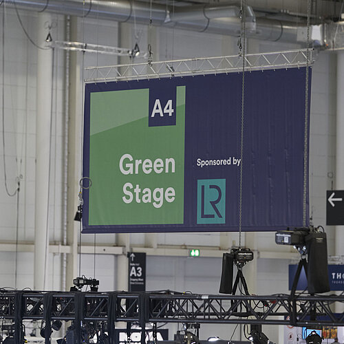 Ein Plakat mit der Aufschrift "A4 Green Stage", das von der Decke hängt, ist zu sehen.