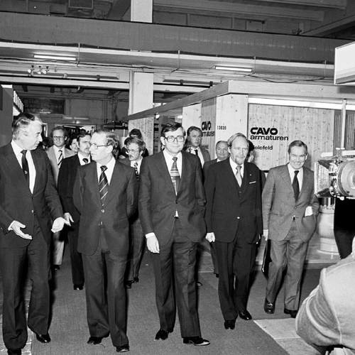 A group of men in suits at a fair. They're being photographed by a photographer to the right.