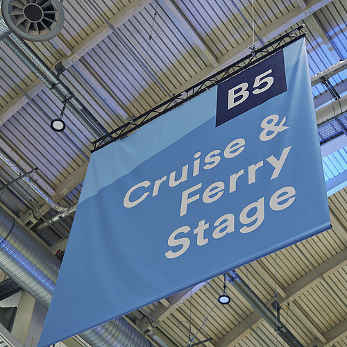 Großes, blaues Plakat, das von der Decke der Halle B5 hängt, mit der Aufschrift ‚Cruise & Ferry Stage‘.