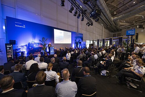 Blick von hinten auf das Publikum der Digital & Security Stage (B6) der SMM 2024, während ein Mann auf der Bühne spricht und eine Präsentation auf der Leinwand gezeigt wird.