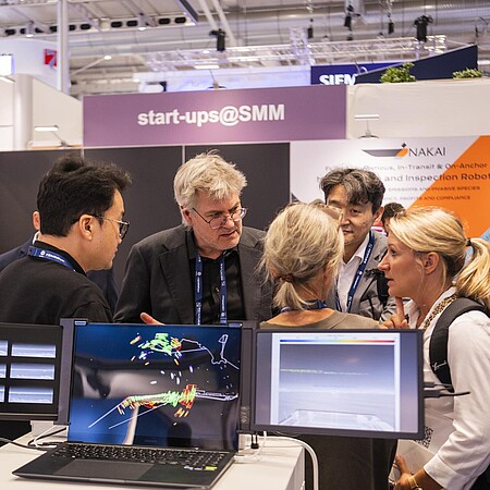 Ausstellende und Besucher unterhalten sich im Start-up Bereich. Es sind einige Bildschirme zu sehen. 