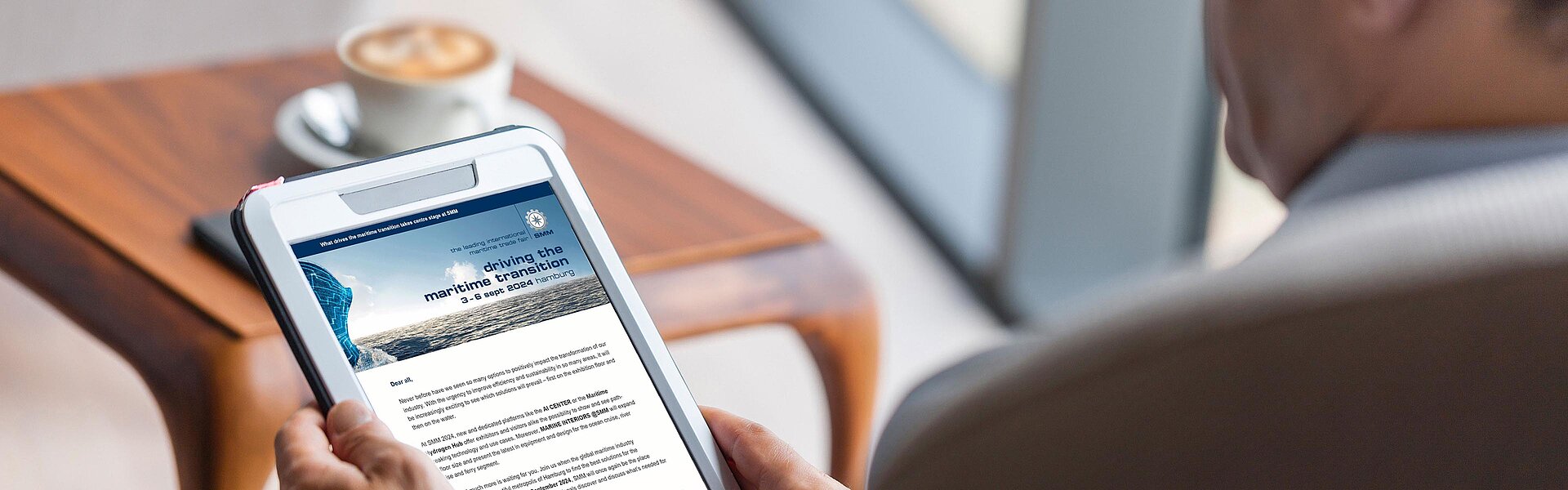 View of a tablet over the shoulder of a man. The tablet shows the SMM news.