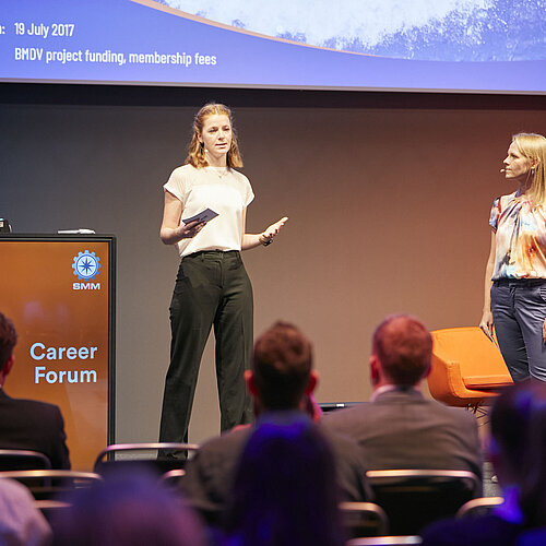 Zwei Frauen stehen vorne auf der Bühne im Career Forum. Bild wurde hinter dem Publikum aufgenommen. 