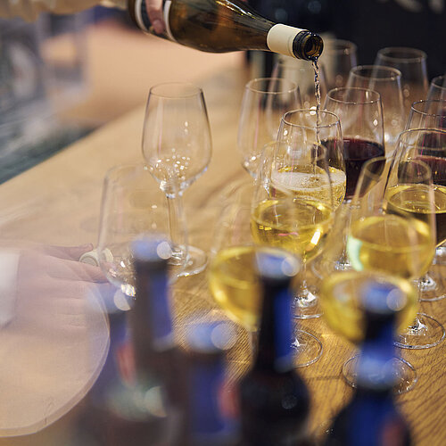 Nahaufnahme von Sekt- und Weingläsern, in denen was eingeschenkt wird. 
