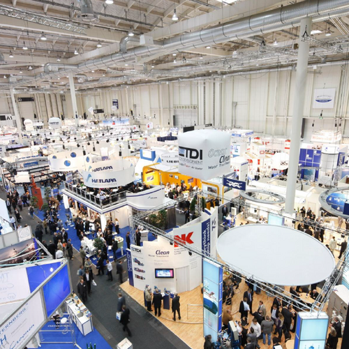An aerial view of a trade fair hall with numerous exhibition stands and visitors